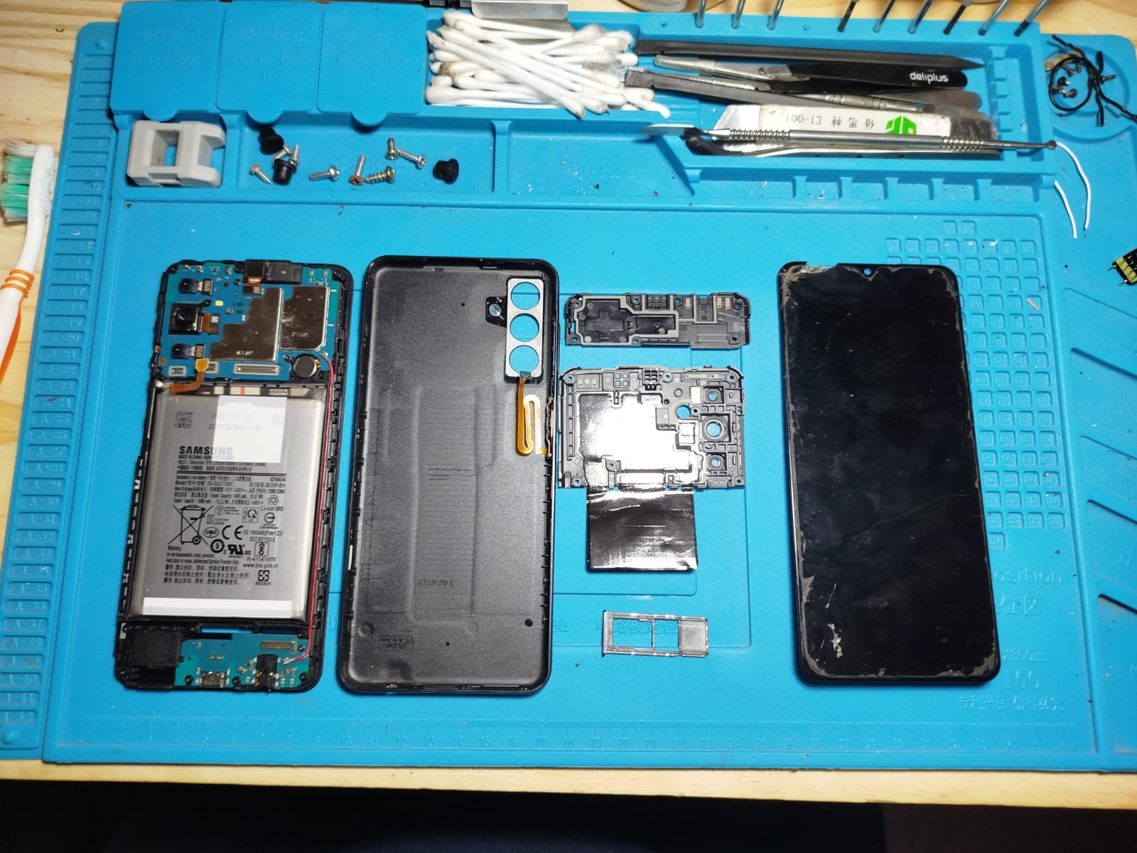 Celular abierto junto a módulos de pantalla en el banco del taller